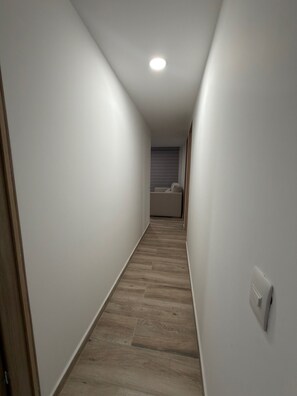 A narrow hallway with wooden flooring, white walls, and a ceiling light.
