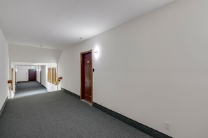 Ein Flur mit Teppichböden, einer Holztür und einem Lichtschalter an der Wand.