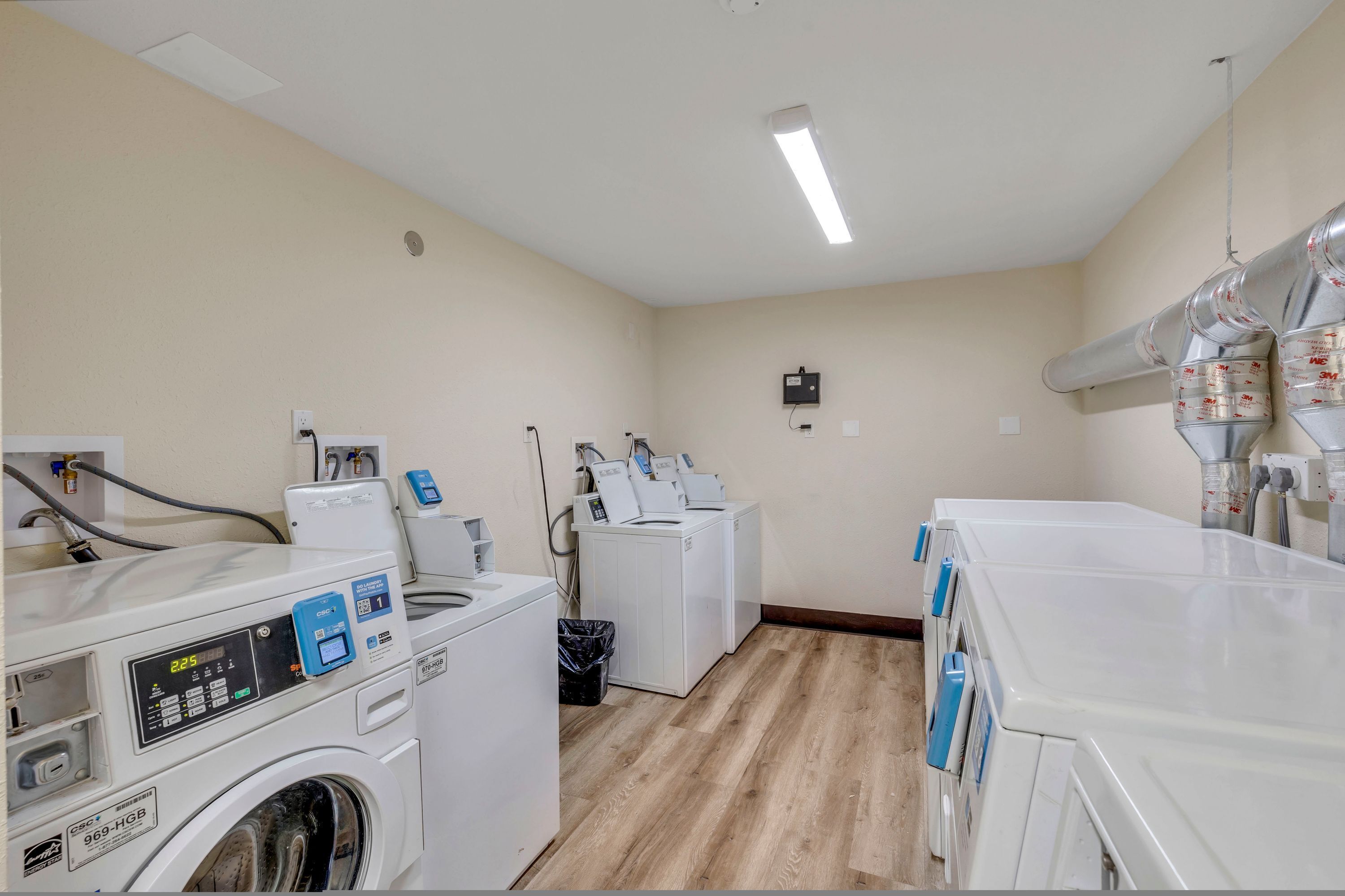 Une buanderie équipée de plusieurs machines à laver et de plusieurs sèche-linge, ainsi que d’une poubelle et d’un chauffe-eau.
