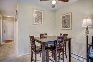 A dining area with a table and chairs, framed artwork on the walls, a ceiling fan, and a lamp. - Wildwood Suites 202 in Breckenridge (Breckenridge)