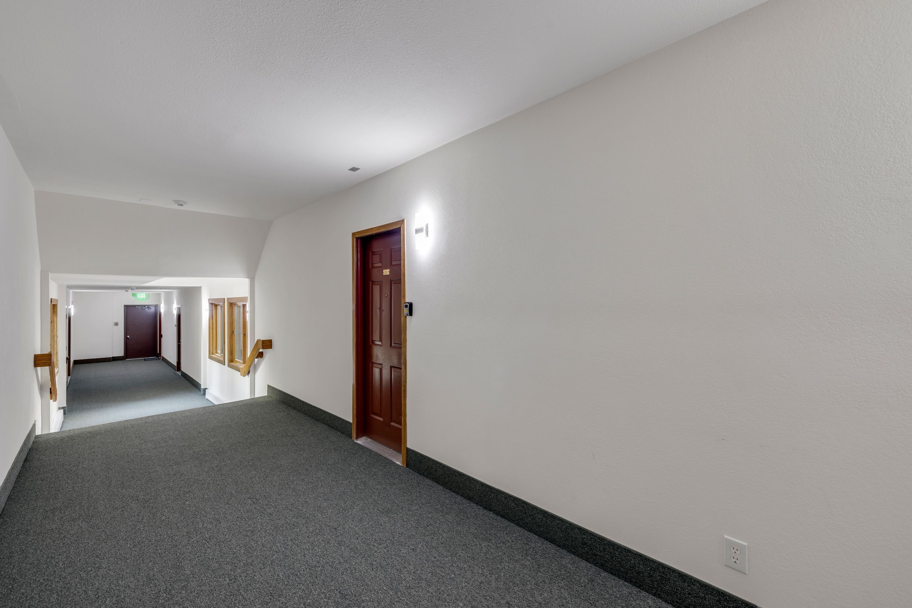 Un couloir avec un sol recouvert de moquette, une porte en bois et un interrupteur sur le mur.
