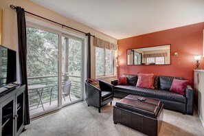 A modern living room with a large sliding glass door, a sofa set, a television, and a fireplace. - Wildwood Suites 202 in Breckenridge (Breckenridge)