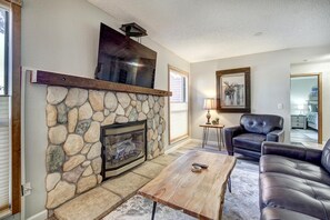 A living room with a stone fireplace, leather sofa, and a mounted television. - Base 9 B101 in Breckenridge (Breckenridge)