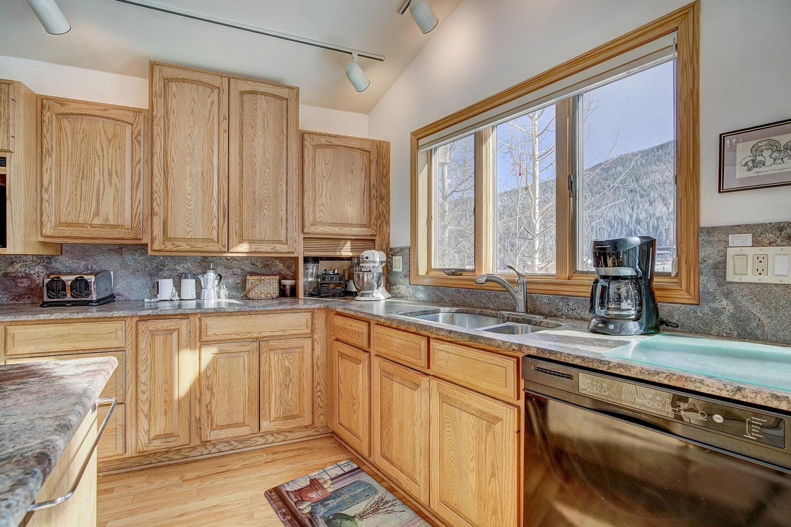 A kitchen with wooden cabinets, a large window, a dishwasher, and a coffee maker.