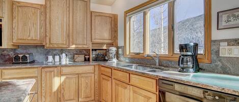 A kitchen with wooden cabinets, a large window, a dishwasher, and a coffee maker.