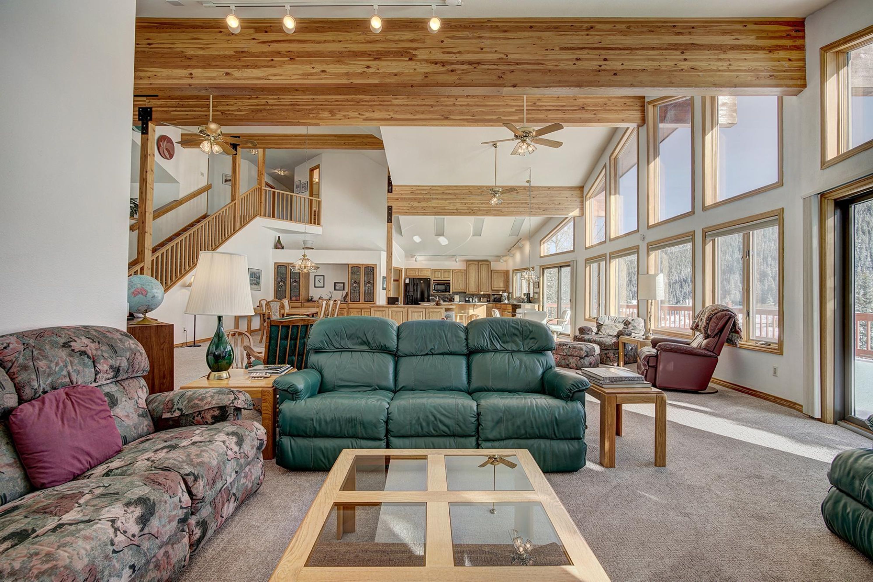 Un vaste espace de vie agrémenté d’un canapé vert, d’une table basse en bois et d’un escalier menant à l’étage supérieur.