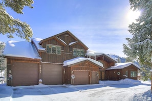 A large wooden cabin with multiple garage doors, surrounded by snow-covered trees and mountains. - Evan's Mountain Lodge (Blue River)