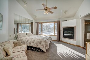 A bedroom with a bed, a sofa, a fireplace, and large windows. - Evan's Mountain Lodge (Blue River)