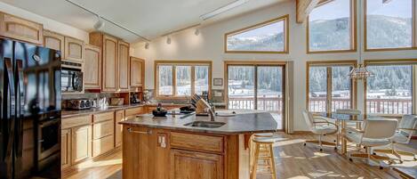A spacious kitchen with wooden cabinets, a large island, and a view of snowy mountains through large windows.
