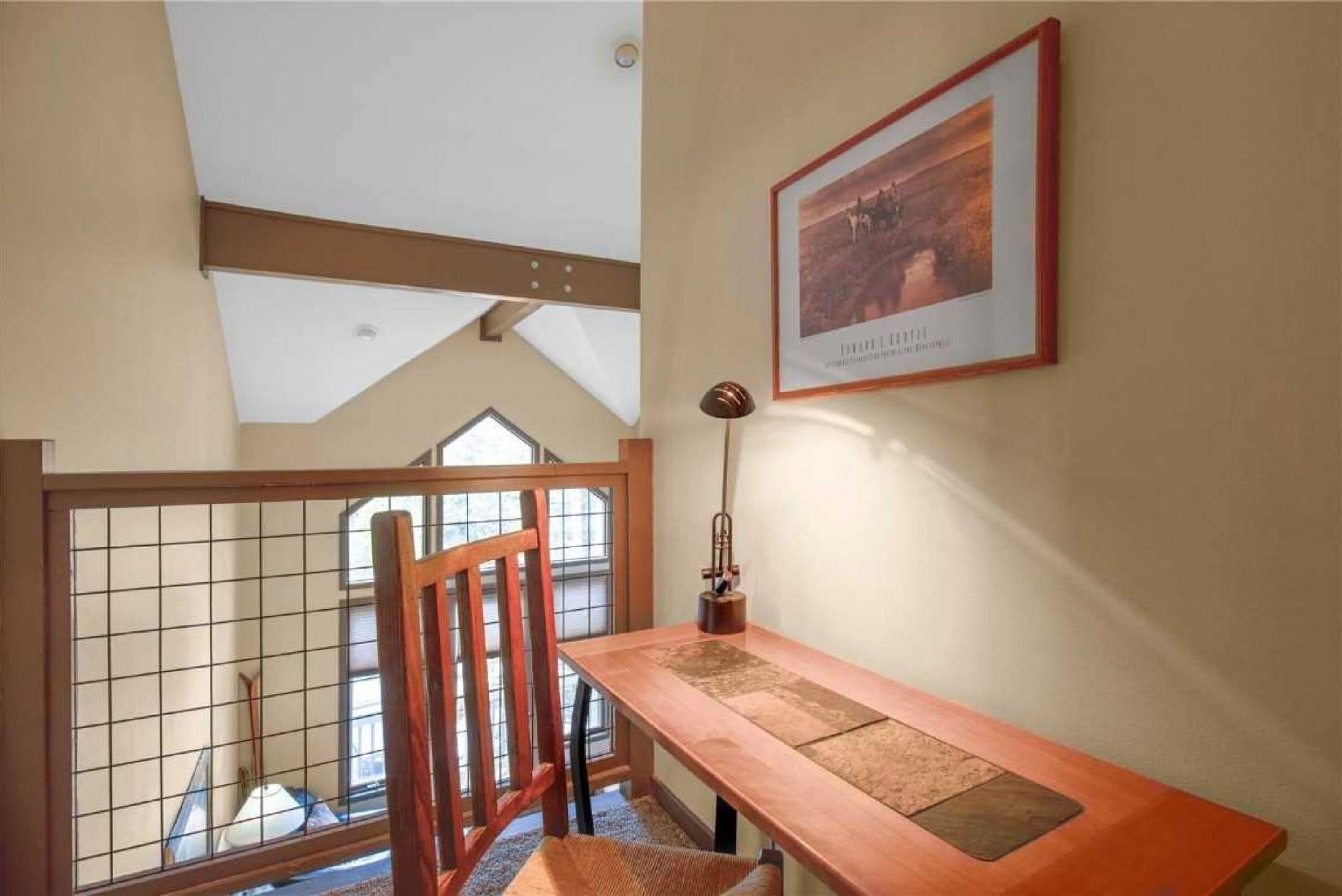A room with a wooden chair, a table, a framed picture on the wall, and a window with a view.