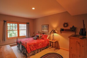 Une chambre à coucher comprenant un lit, une table de chevet, une lampe, une commode, une fenêtre avec des rideaux et un tableau accroché au mur.