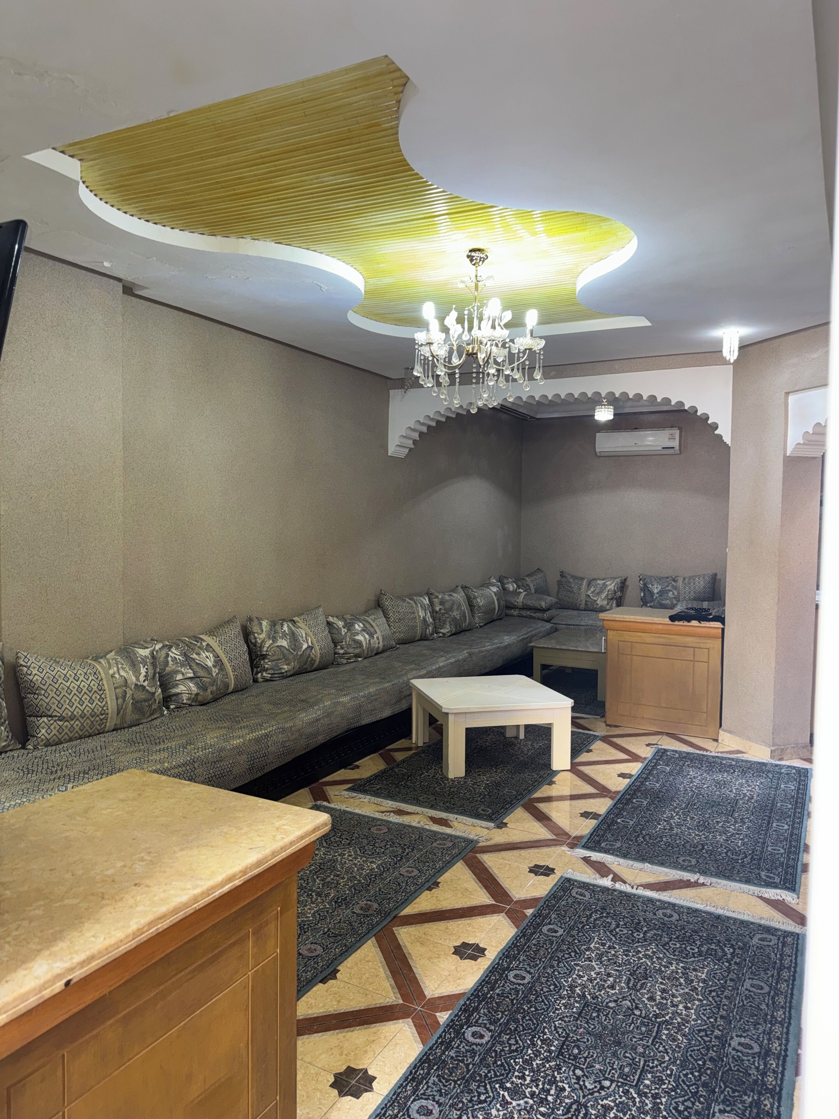 Ein Wohnzimmer mit einer Couch, einem Couchtisch, gemusterten Teppichen, einer Deckenleuchte und einem außergewöhnlichen Deckenmuster.
