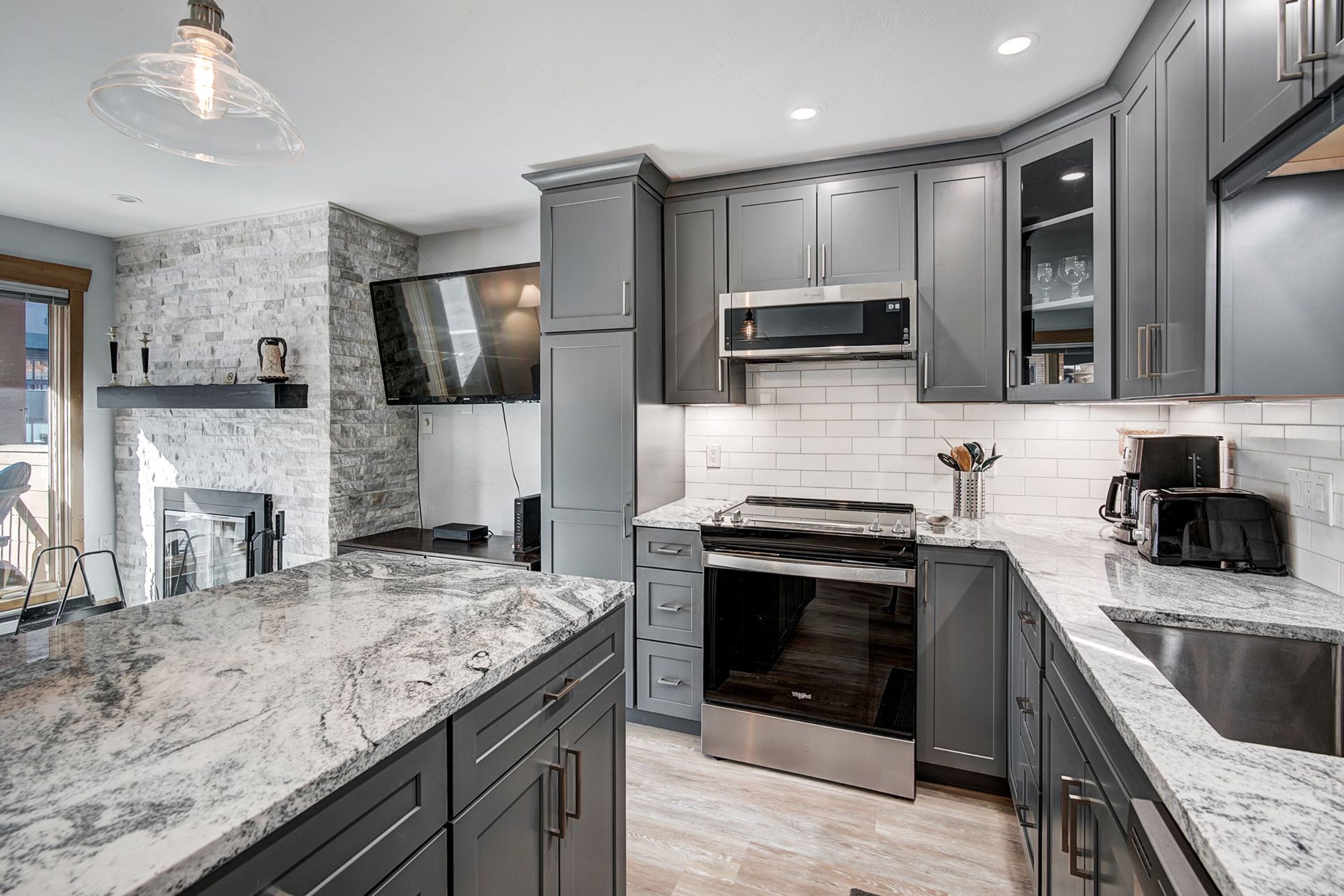 A modern kitchen with grey cabinets, a built-in microwave, and a large island with a marble countertop.