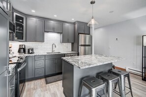 A modern kitchen with grey cabinets, a stainless steel refrigerator, a marble countertop, and a hanging pendant light. - Der Steiermark 104 in Breckenridge (Breckenridge)
