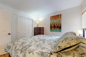A bedroom with a bed, a nightstand, a lamp, and a painting on the wall. - Wildwood Suites 107 in Breckenridge (Breckenridge)
