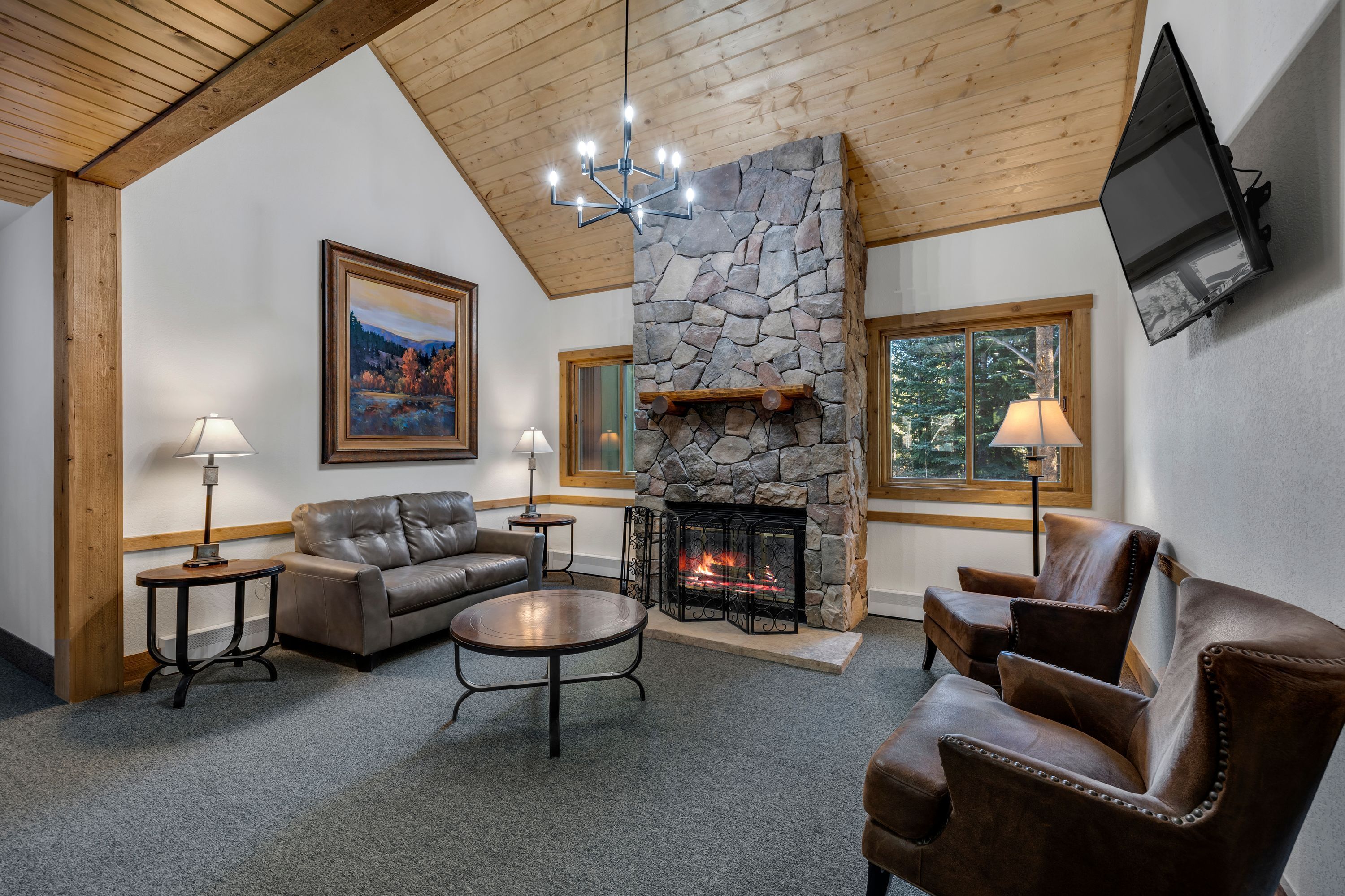 Una sala de estar acogedora con chimenea de piedra, muebles de cuero y televisor montado.