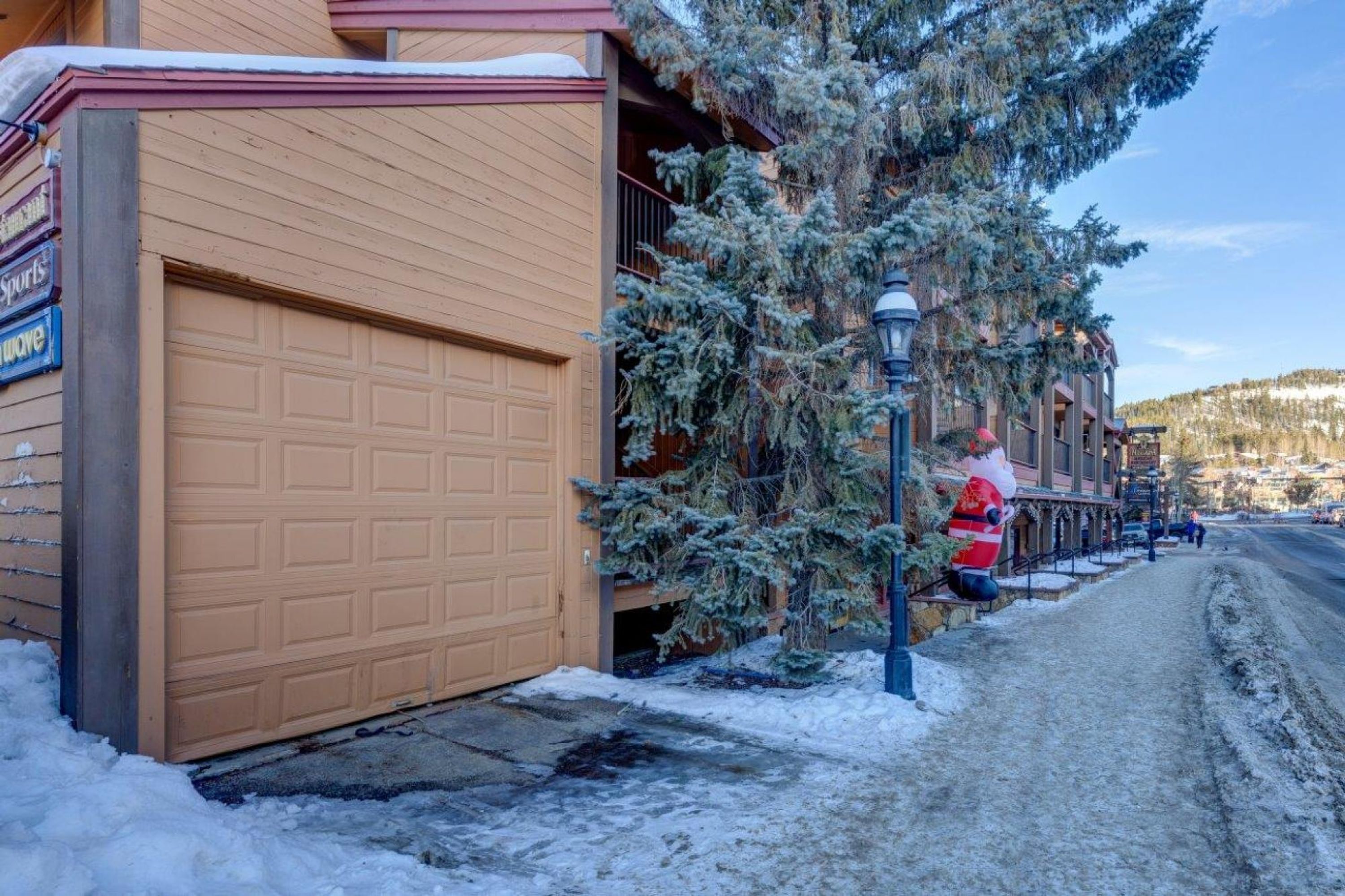 A residential street with a garage door, a snow-covered tree, and a pedestrian walkway.