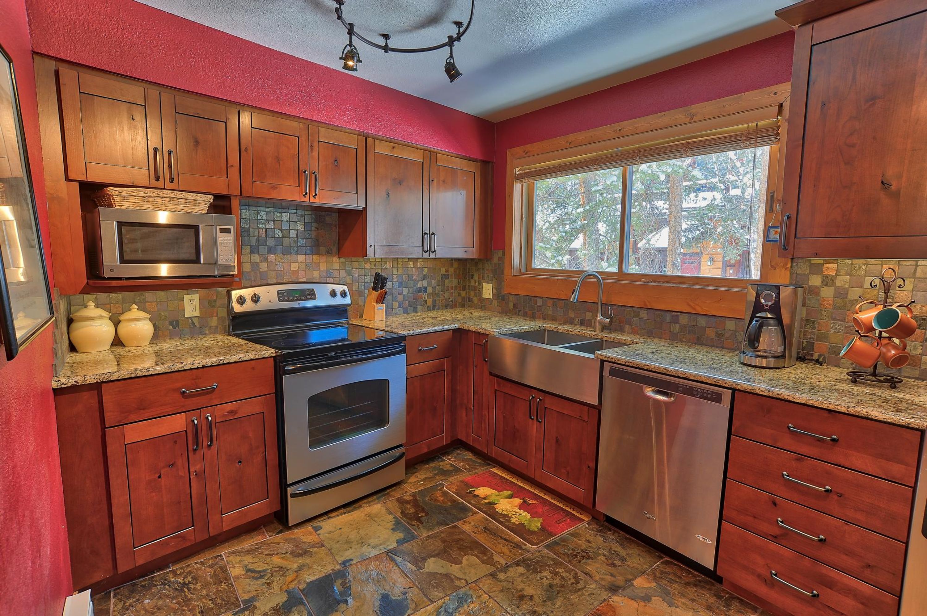 A kitchen with wooden cabinets, a microwave, stove, sink, and a window with a view of trees.
