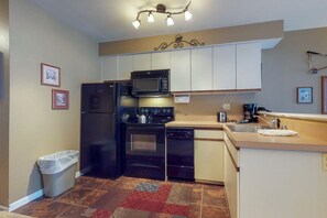 A compact kitchen with a refrigerator, microwave, stove, and dishwasher. There is a trash bin and a sink with a towel. - Wildwood Suites 101 in Breckenridge (Breckenridge)