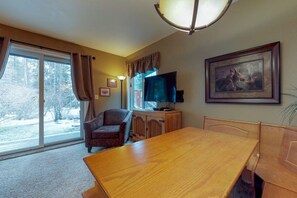 A room with a large window, a dining table, a television, and a framed picture on the wall. - Wildwood Suites 101 in Breckenridge (Breckenridge)