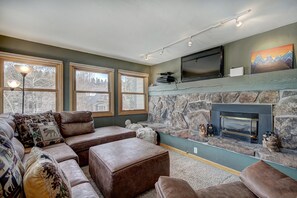 A living room with a stone fireplace, a large flat-screen TV mounted above it, and a sectional sofa with multiple cushions. - Longbranch 201 in Breckenridge (Breckenridge)