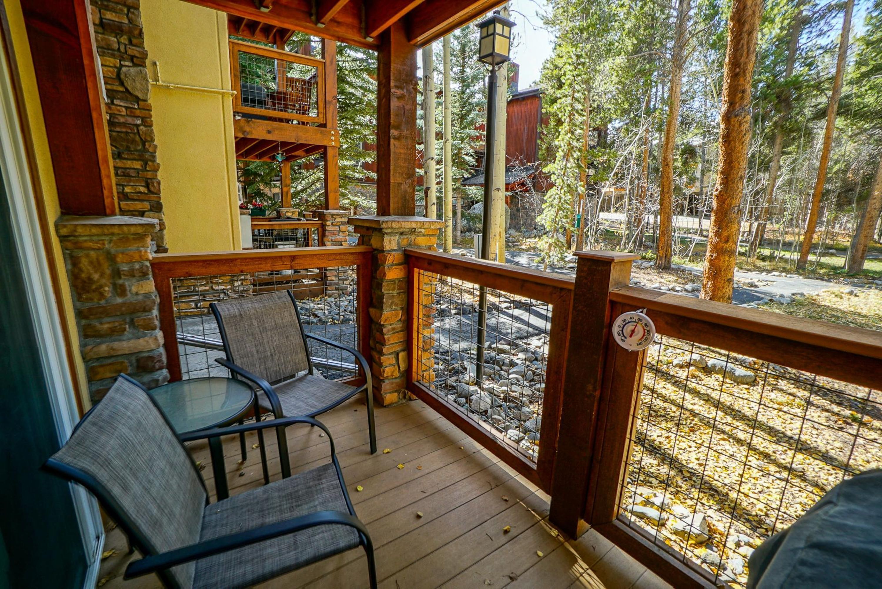 A covered outdoor seating area with stone walls, a wooden deck, and a view of a rocky stream.