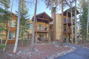 Un bâtiment à étages, de style chalet, avec une façade en pierre, des balcons en bois et un espace boisé qui l’entoure.