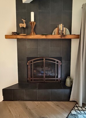 A fireplace with a dark tiled surround, a wooden mantel shelf with decorative items, and a rug on the floor. - Columbine 108 in Breckenridge (Breckenridge)