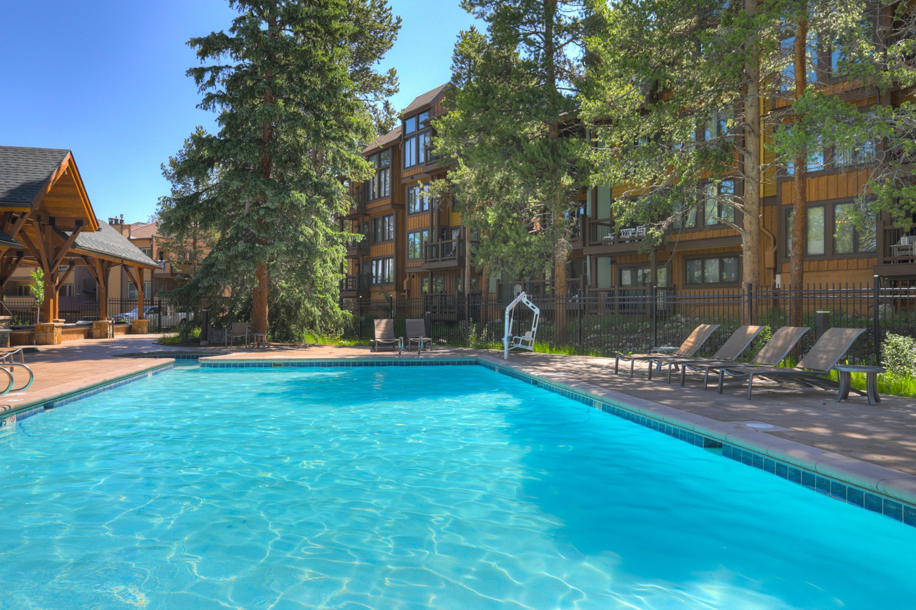 A swimming pool with lounge chairs, surrounded by multi-story buildings with large windows and trees.
