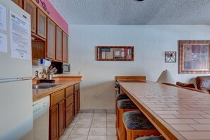 Cuina amb armaris de fusta, respatller de rajoles, zona de bar amb tamborets i taula de menjador.