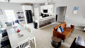 Une cuisine moderne avec des meubles blancs, un réfrigérateur noir et un coin repas comprenant une table et des chaises blanches.
