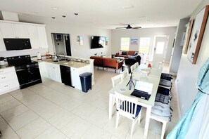 A modern kitchen with a central island, a dining area with a table and chairs, a living room with a sofa, and a ceiling fan. - House w/Private Pool/Near Beach+Attractions (Panama City)