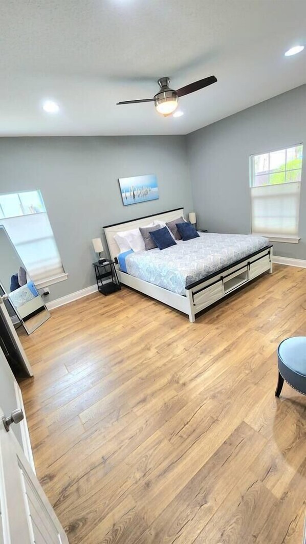 Ein Schlafzimmer mit Bett, Deckenventilator, Nachttisch, Fenster und Tür.