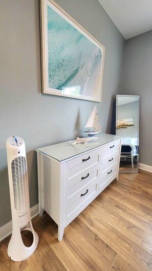 Een kamer met een witte dressoir, een elektrische kachel, een lijst met abstracte kunst en een spiegel.