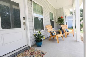 Eine Veranda mit zwei Holzstühlen, einem Blumentopf und einer Fußmatte.