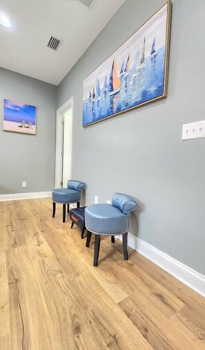 A hallway with a wooden floor, a painting of sailboats, and a door.