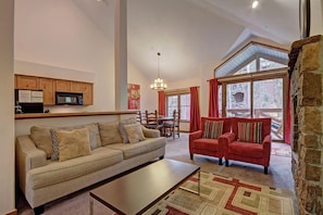 A living room with a sofa, a red couch, a dining table, and a kitchen area with cabinets and a microwave. - Los Pinos D-24 in Breckenridge (Breckenridge)