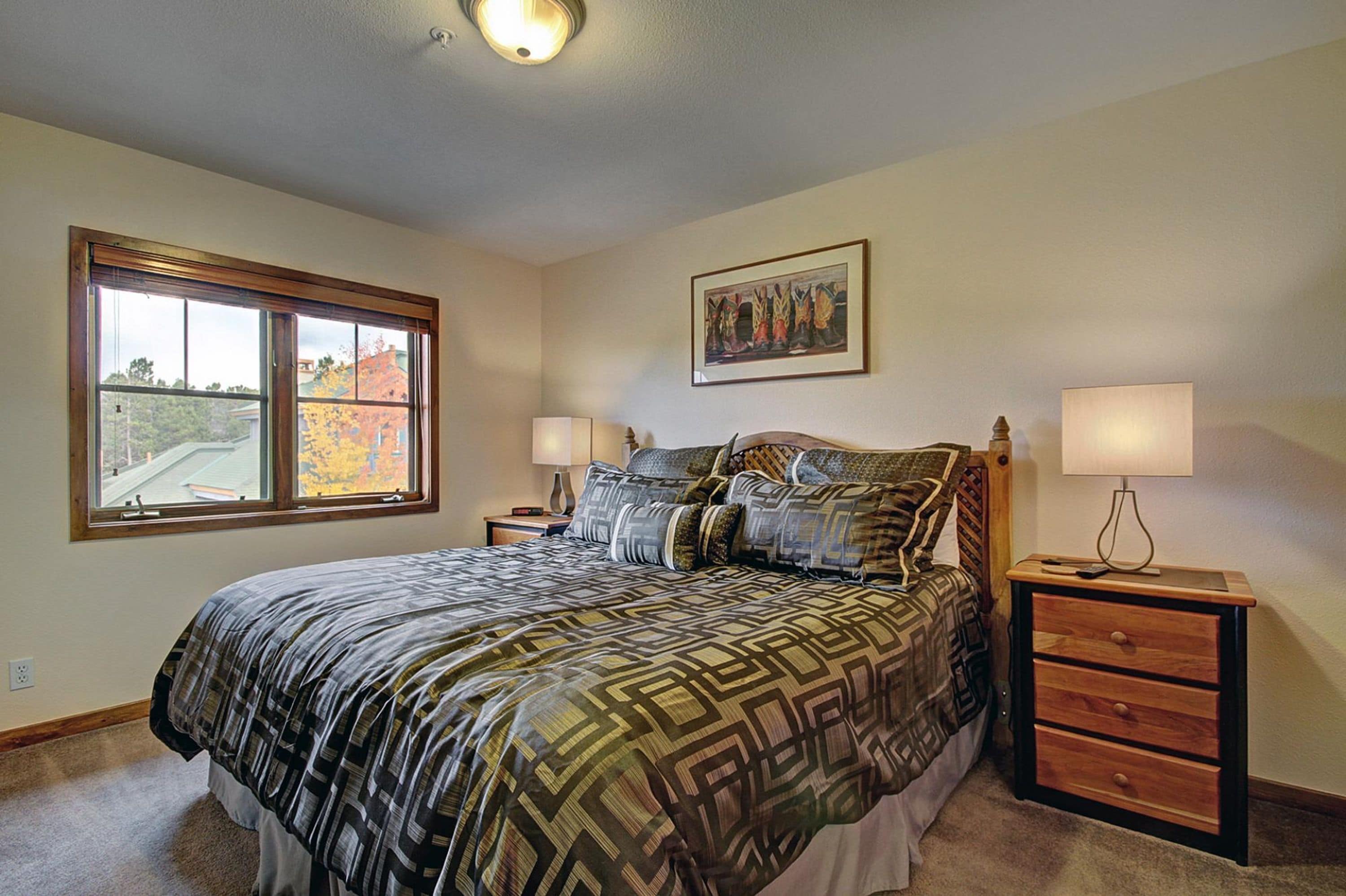A bedroom with a large bed, two bedside tables, a window, and a painting on the wall.