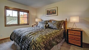 A bedroom with a large bed, two bedside tables, a window, and a painting on the wall. - Los Pinos D-24 in Breckenridge (Breckenridge)