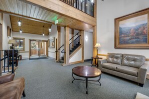 Un hall d’entrée spacieux avec un plafond haut, un escalier, un canapé en cuir et un grand tableau accroché au mur.