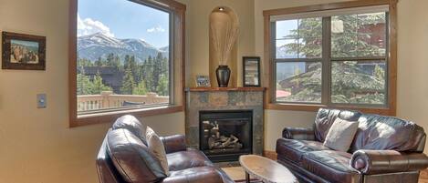 A living room with leather sofas, a fireplace, and large windows with mountain views.