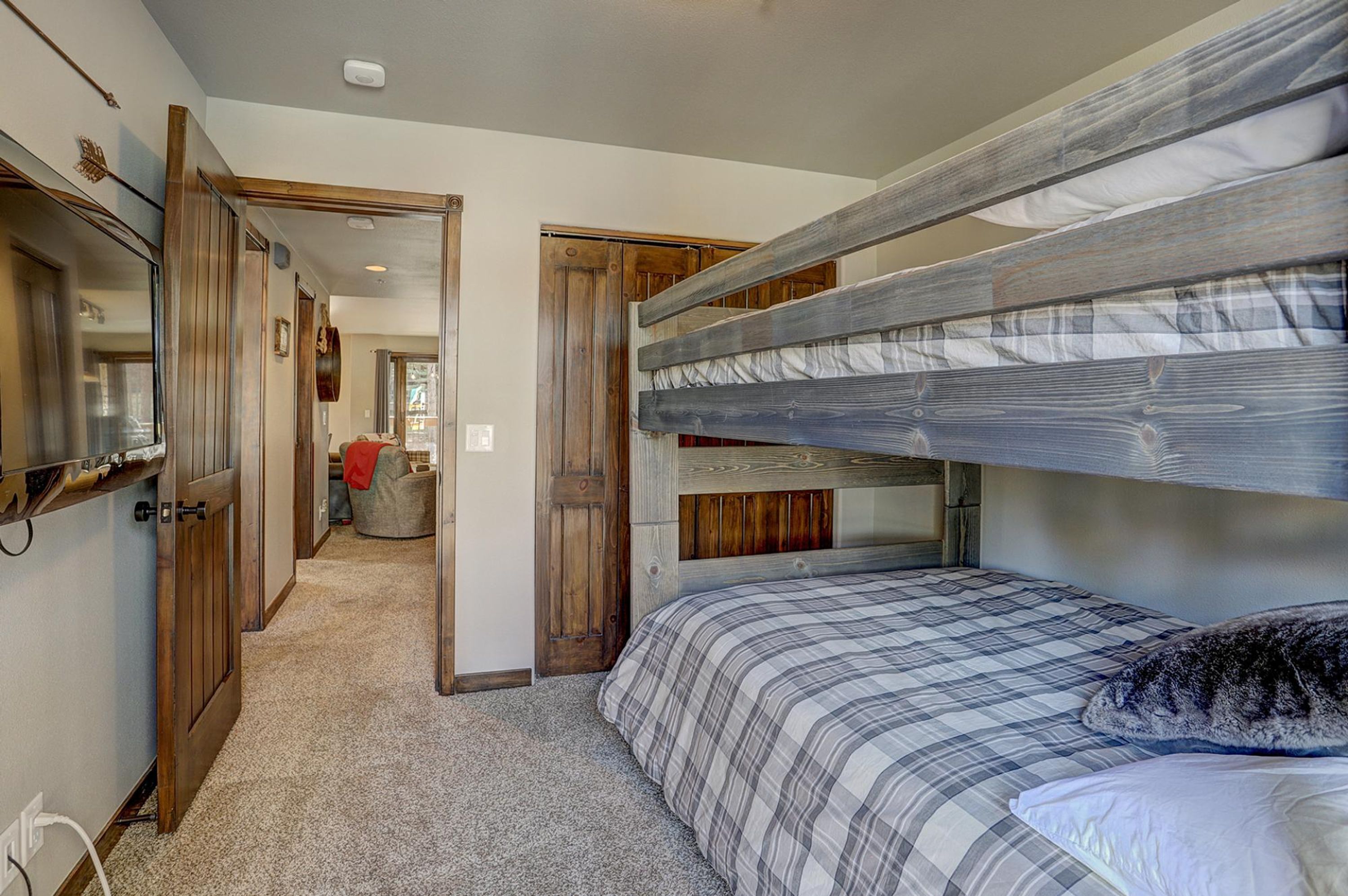 A bunk bed with a checkered bedspread, a wooden headboard, and a mirror on the left wall.