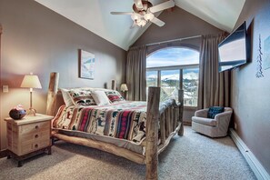 A bedroom with a bed, a nightstand, a chair, a ceiling fan, a window with curtains, and a TV mounted on the wall. - Liftside Retreat in Breckenridge (Breckenridge)