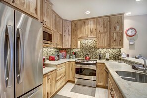 A kitchen with wooden cabinets, stainless steel appliances, a tiled backsplash, and a clock on the wall. - Liftside Retreat in Breckenridge (Breckenridge)