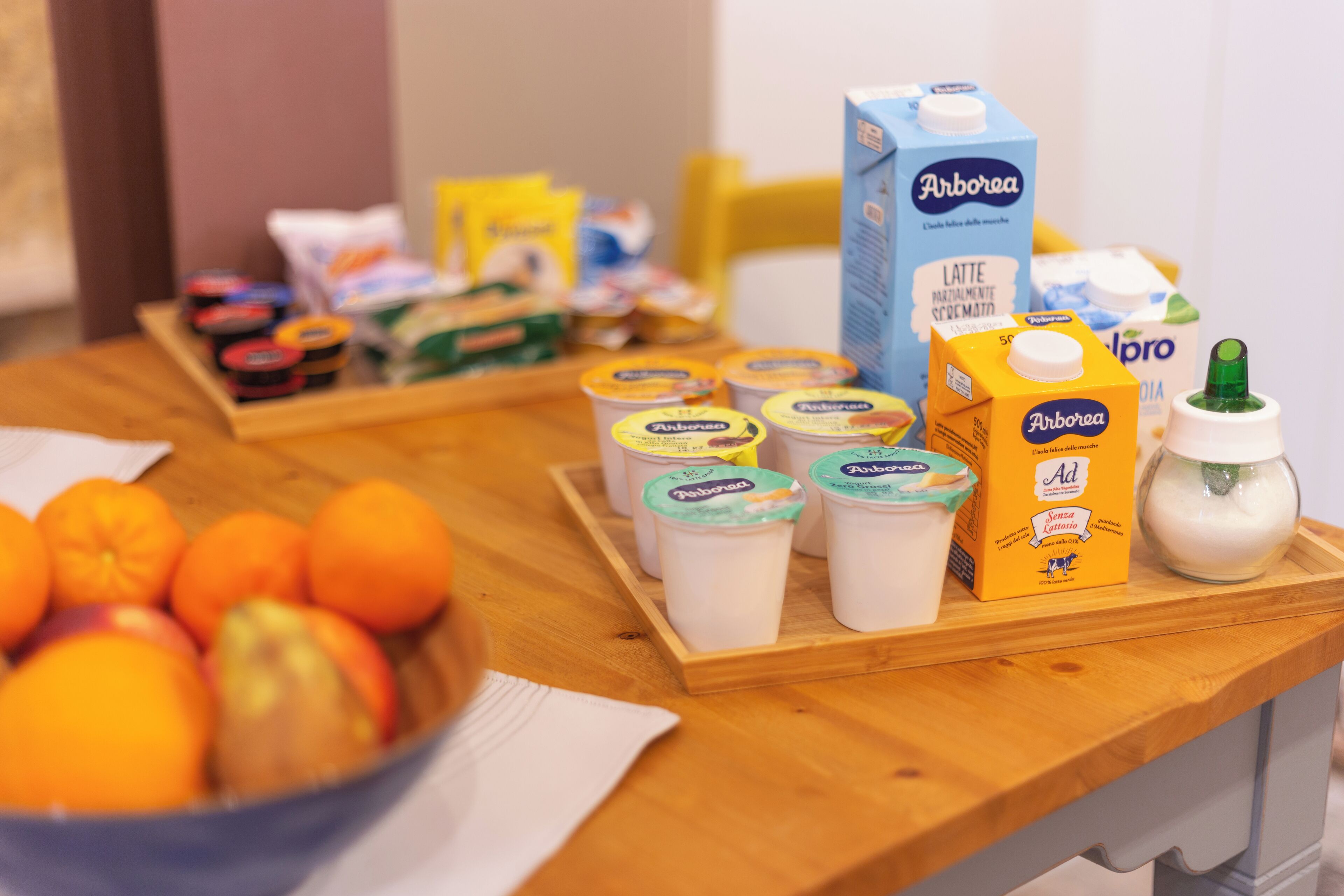 Una tavola per la colazione con diversi cibi e bevande, tra cui una ciotola di frutta, succhi di frutta e latte in brick.