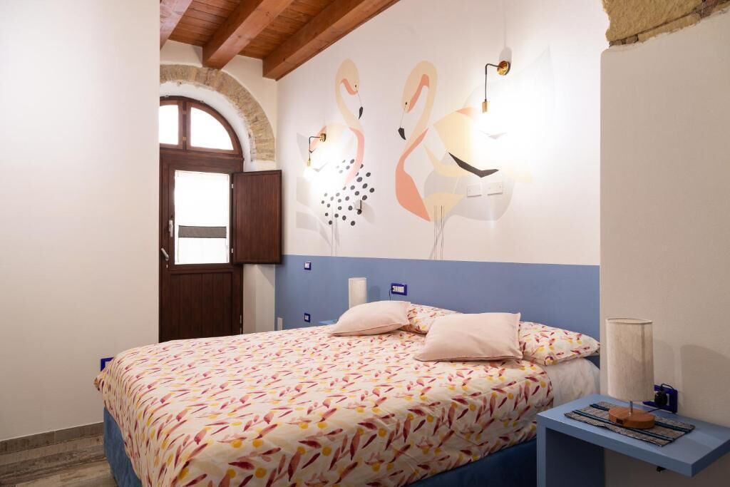 Un dormitorio con cama, mesita de noche, lámpara de pared y puerta.