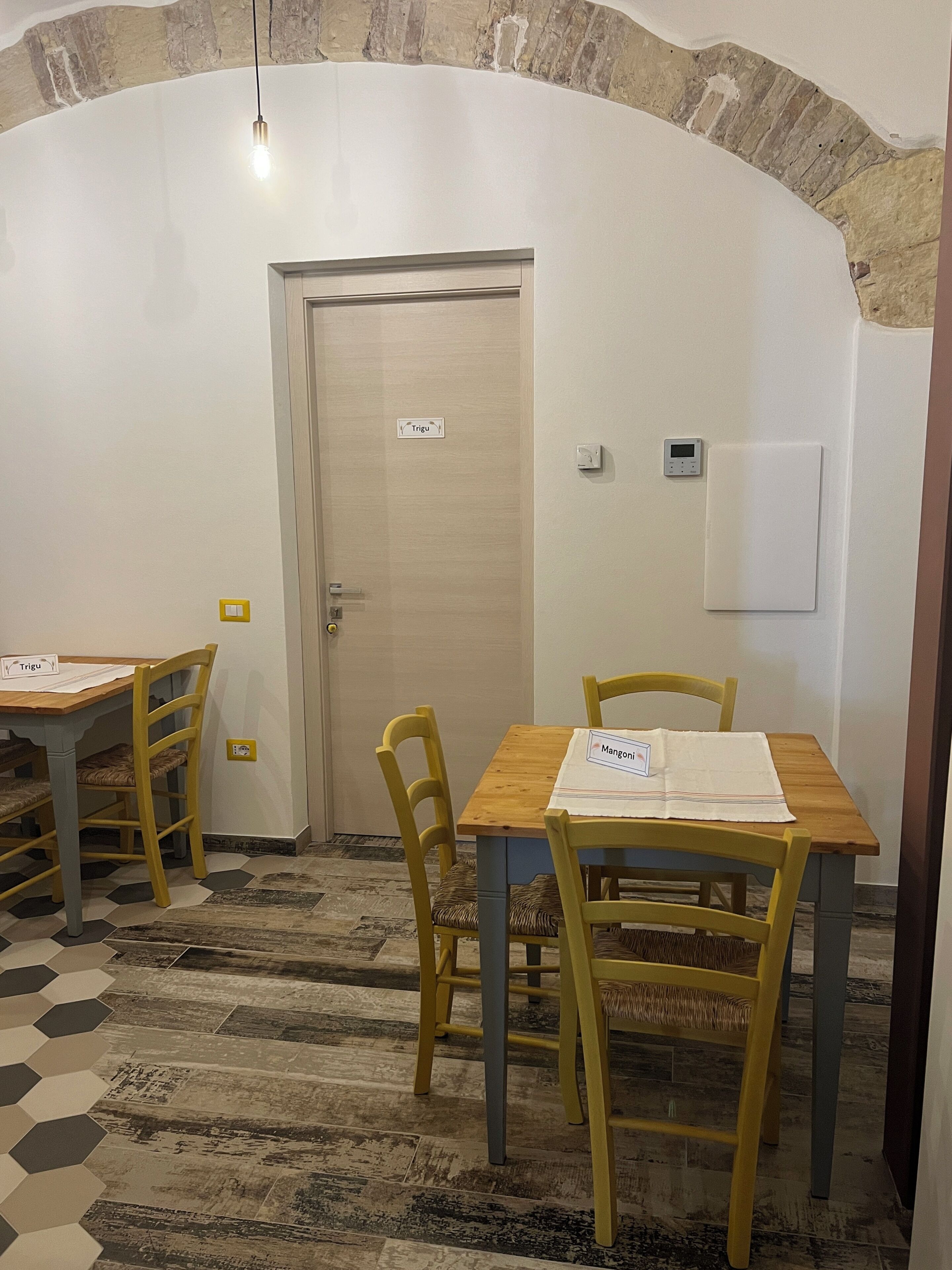 Una habitación con una mesa y sillas de madera, una puerta con un cartel, un termostato y una pared con textura.