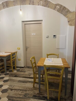A room with a wooden table and chairs, a door with a sign, a thermostat, and a textured wall.