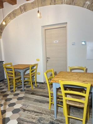 A dining area with two wooden tables and yellow chairs, a white door with a nameplate, and a stone archway. - Trigu & Mangoni (Cagliari)