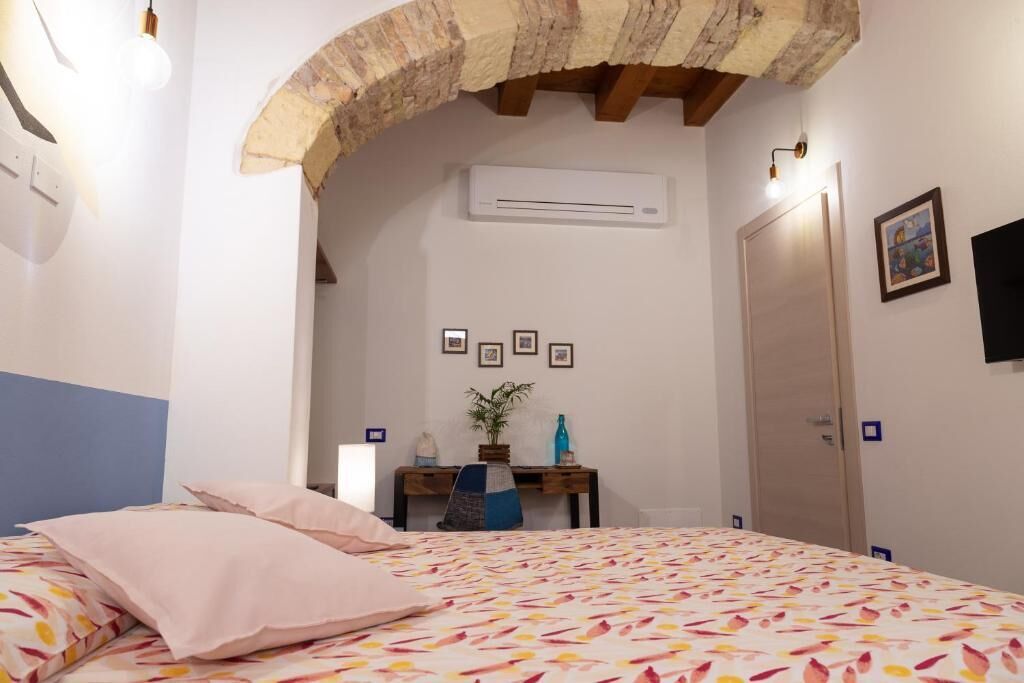 A bedroom with a bed, a desk, a chair, an air conditioning unit, and a door.